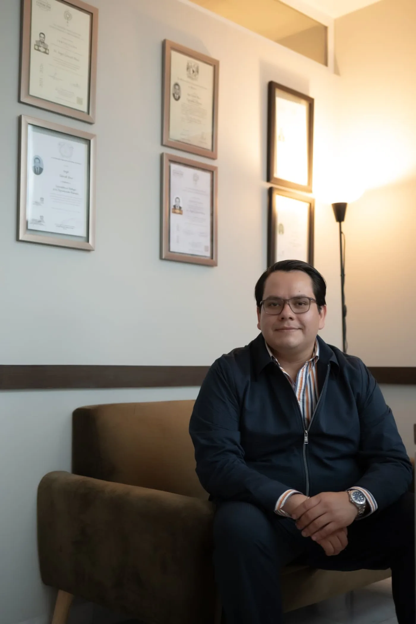 Dr. Ángel Zistecatl Meza sentado en su consultorio frente a sus diplomas de especialidad